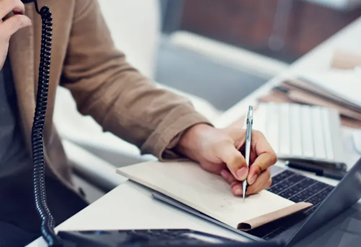 pracownik biurowy rozmawiający przez telefon i robiący notatki